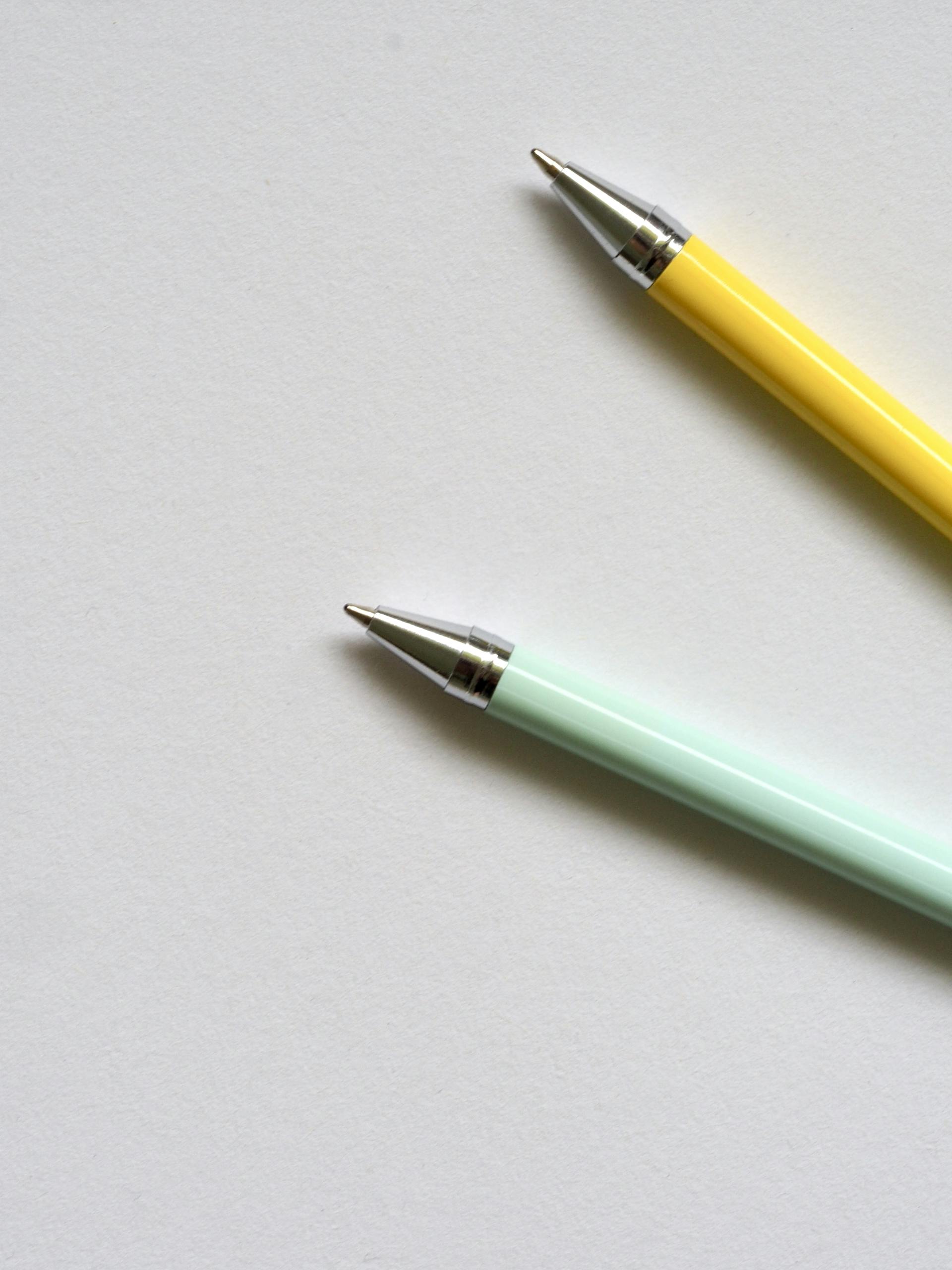 Minimalist shot of two colorful ballpoint pens on a plain white surface. Perfect for office or school themes.